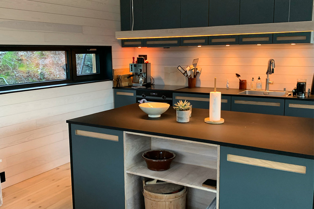 Bilde av kjøkken på hytta til finalist nummer 1 i hytterprisen 2022. Kvistfritt panel som er hvitlasert går igjen i hele hytta. 