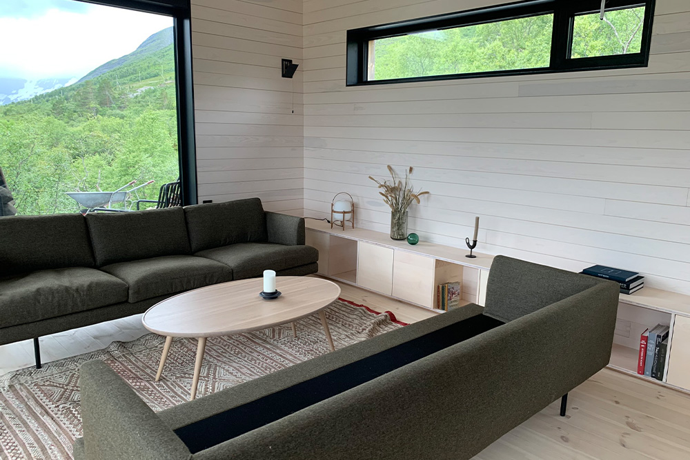 Bilde av sofakrok på hytta hos finalist nummer 1 i hytterprisen 2022. Kvistfritt panel som er hvitlasert går igjen i hele hytta. 